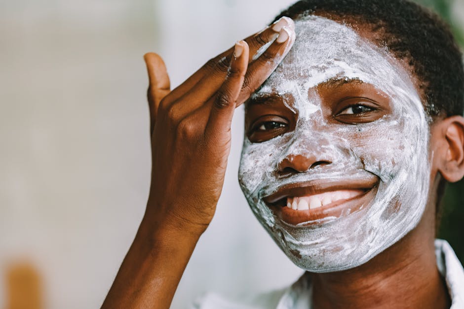 A black woman joyfully applying skincare cream to her face indoors.
