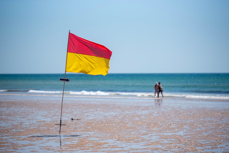 Red and yellow beach safety flag in the foreground with an ocean view, indicating safe swimming area.