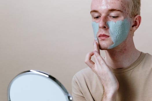Close-up of a young man applying a clay face mask with a mirror.