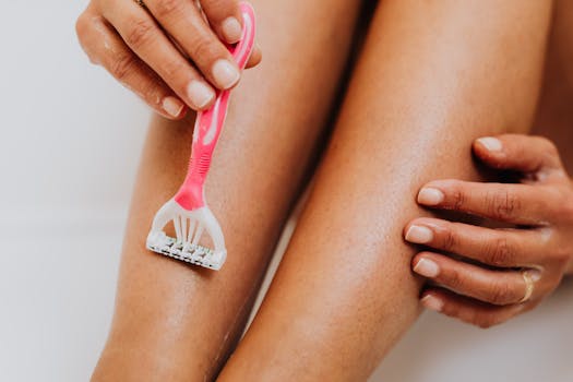 A close-up image of a person shaving their leg with a pink razor, focusing on smooth skin and personal care.