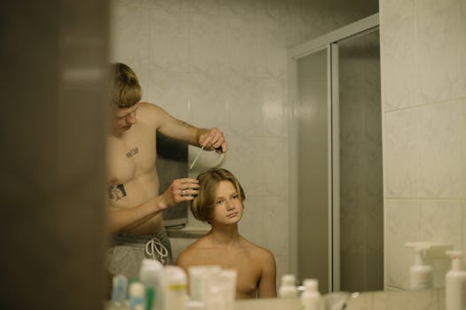 A young tattooed man combs his hair by a bathroom mirror, focusing on grooming.