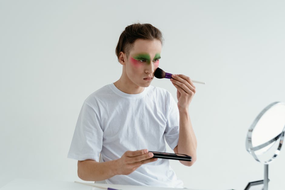 A young man applies vibrant eyeshadow in a modern style using a makeup brush indoors.