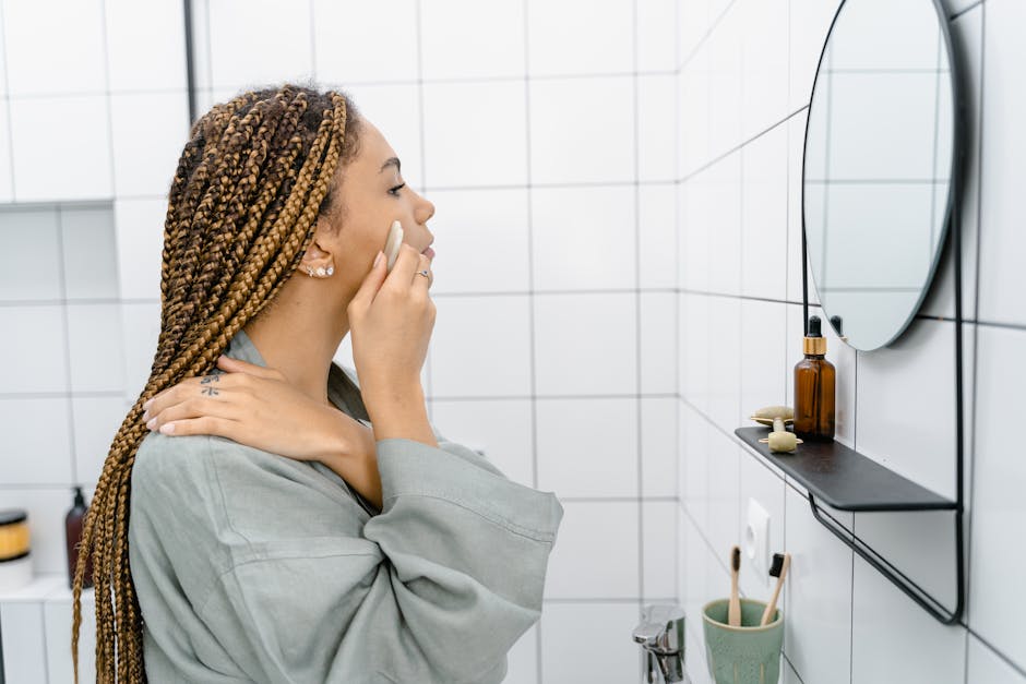 Woman applying skincare in a bathroom while looking at the mirror, focusing on self-care.