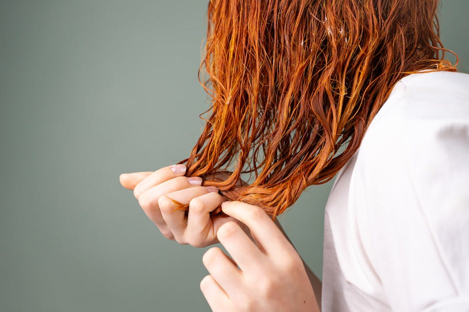 A detailed image showing a close-up of red hair being held by delicate hands against a neutral background.